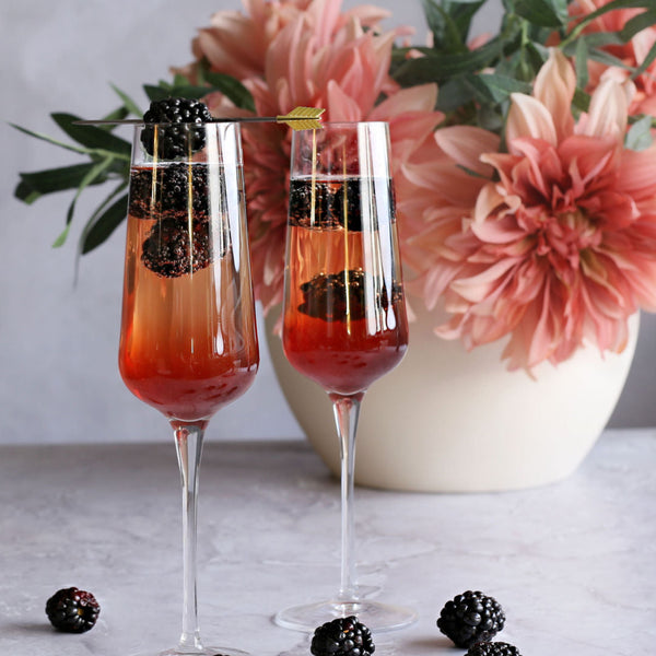 A Blackberry French Kiss cocktail with vodka, Rustic Oak Blackberry Mixer, and champagne, garnished with fresh blackberries in a flute glass.