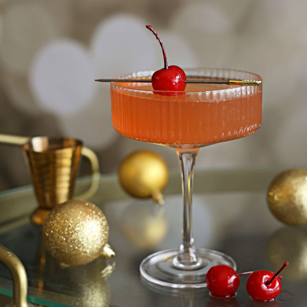 A Cherry French 75 cocktail with gin, lemon, Rustic Oak Sour Cherry Mixer, and champagne, garnished with Luxardo cherries in a flute glass.
