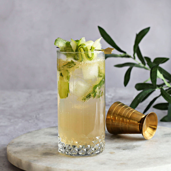 A zero-proof Cucumber Highball with Rustic Oak Traditional Mixer, orange bitters, and tonic water, garnished with cucumber slices.