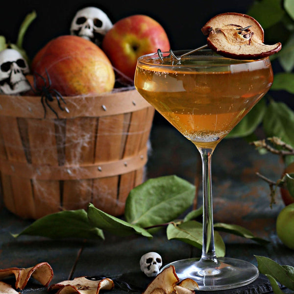 The Haunted Orchard Halloween cocktail with vodka, apple cider, Rustic Oak Traditional Mixer, and prosecco, garnished with an apple chip for a spooky presentation.