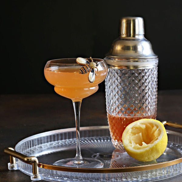 A zero-proof Bee's Knees with honey syrup, lemon juice, Rustic Oak Barrel Aged Mixer, and aromatic bitters, served in a chilled coupe glass.