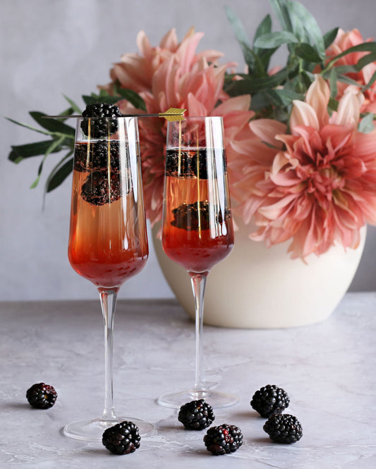 A Blackberry French Kiss cocktail with vodka, Rustic Oak Blackberry Mixer, and champagne, garnished with fresh blackberries in a flute glass.