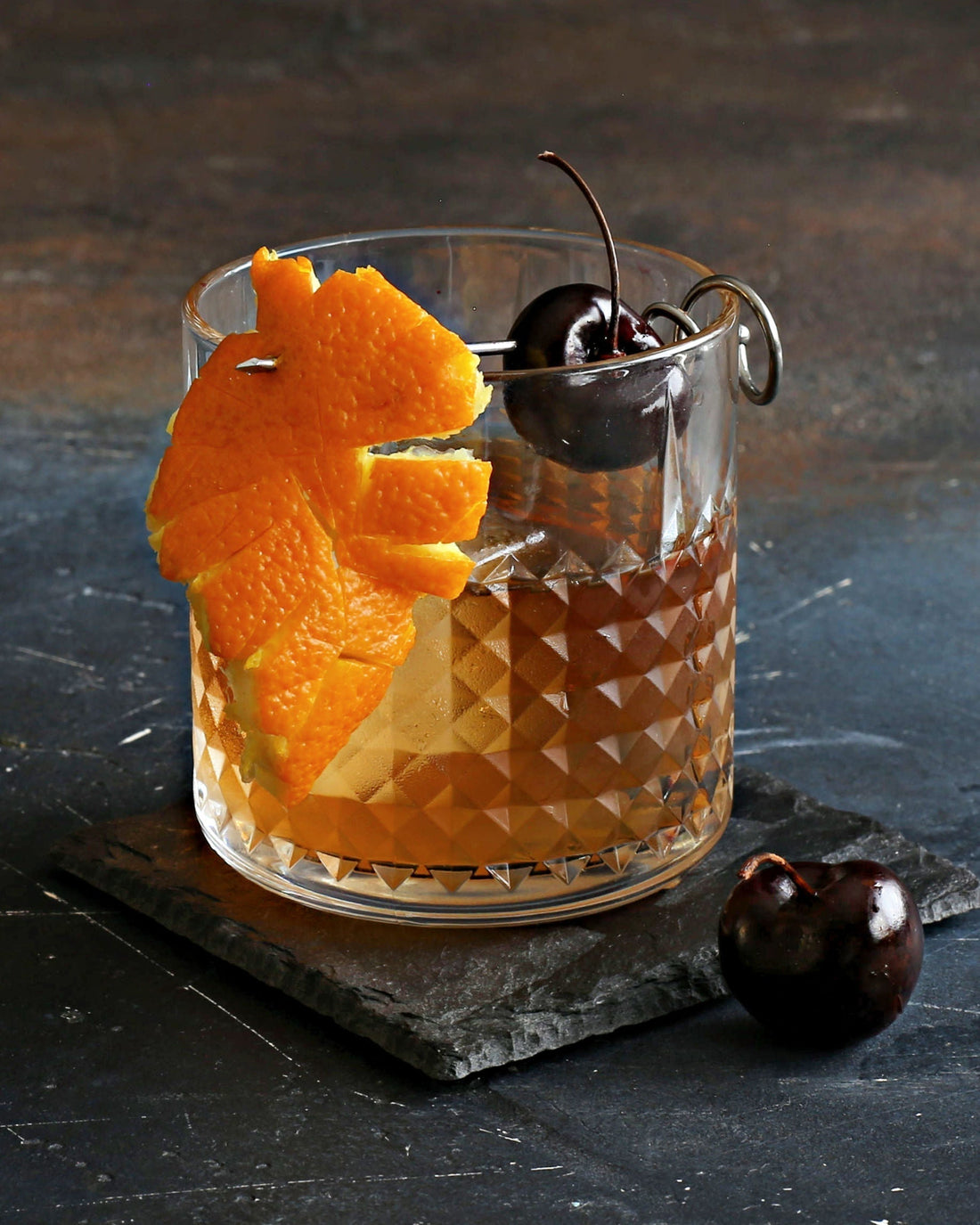Two glasses of a Classic Old Fashioned cocktail with bourbon, Rustic Oak Traditional Mixer, orange peel, and Luxardo cherry garnish on a dark surface.