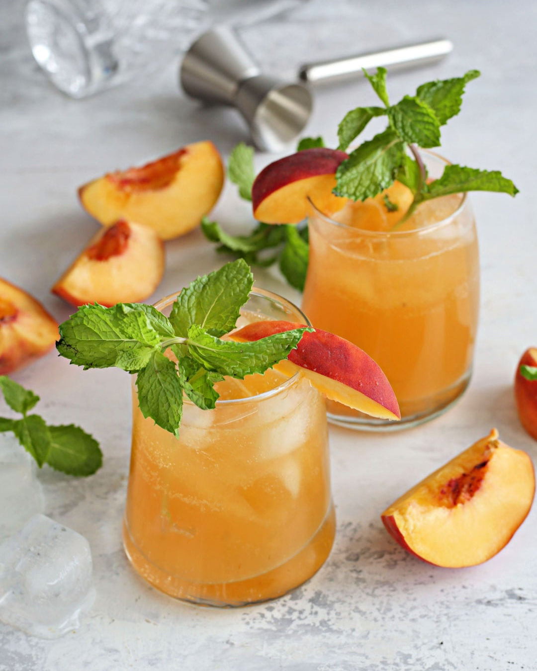 A Bourbon Barrel Peach Smash cocktail with bourbon, Rustic Oak Barrel Aged Mixer, fresh peach, lemon juice, and mint on a textured surface.