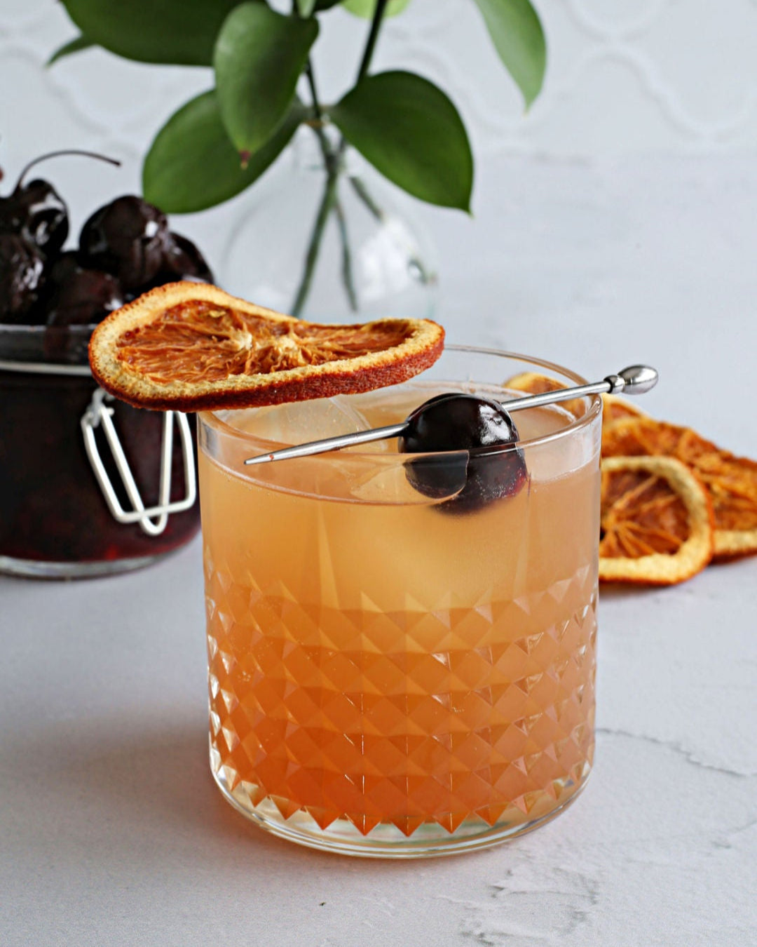 A Cherry Godfather Sour cocktail with scotch, Amaretto, Rustic Oak Sour Cherry Mixer, and lemon juice, garnished with an orange wheel and Luxardo cherry.
