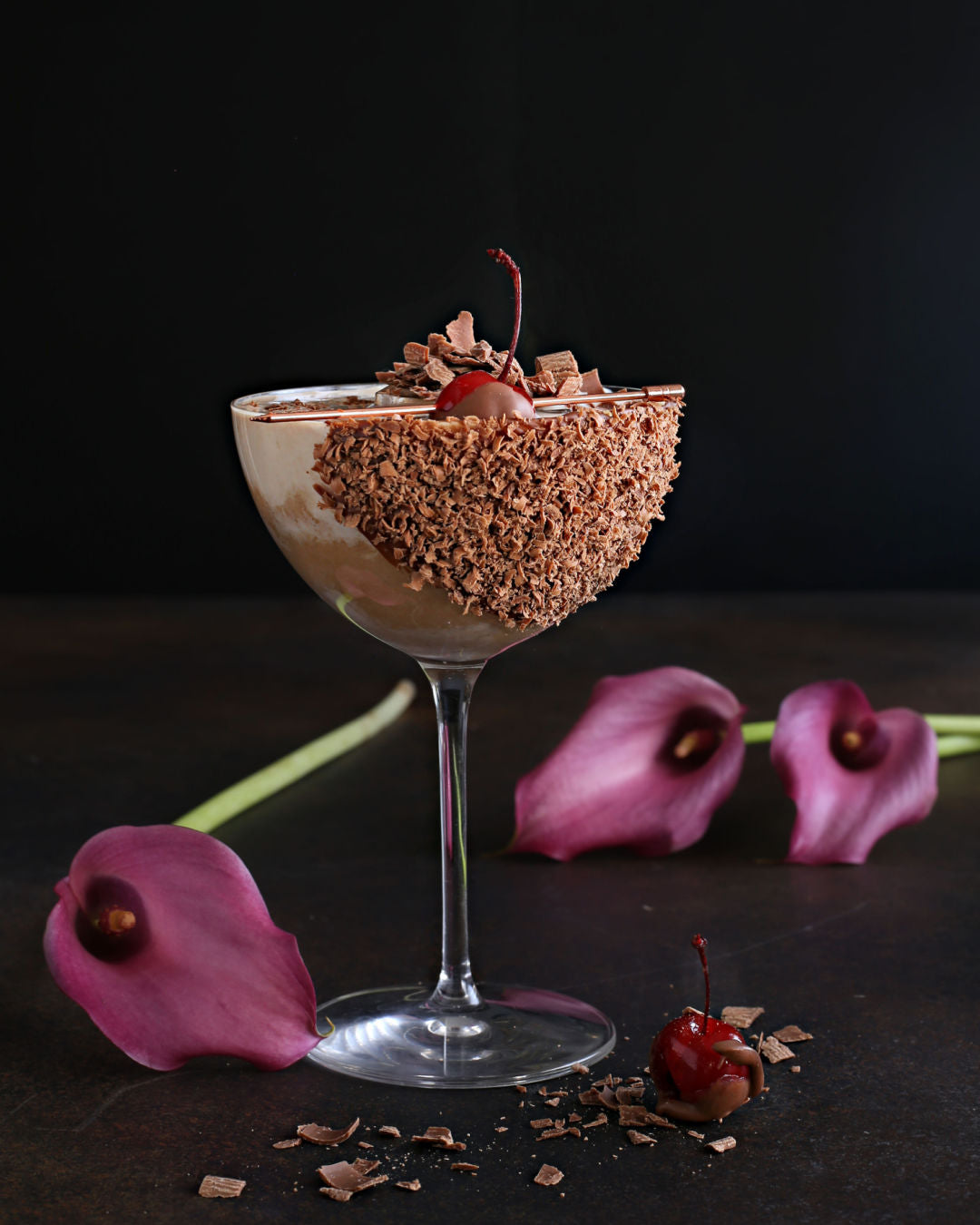 A Chocolate Covered Cherry Martini with vodka, crème de cacao, Rustic Oak Sour Cherry Mixer, served in a chocolate-dipped glass with cherry garnish.