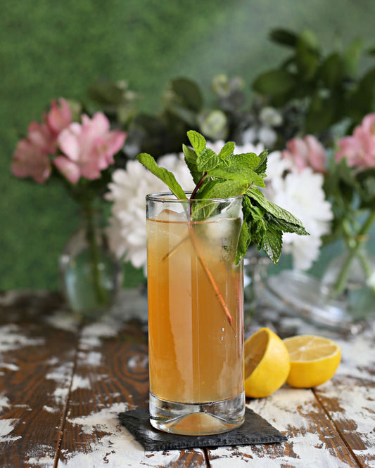 A Garden Party Buck cocktail with bourbon, lemon, Rustic Oak Prohibition Mixer, ginger beer, and fresh mint, served in a tall glass.