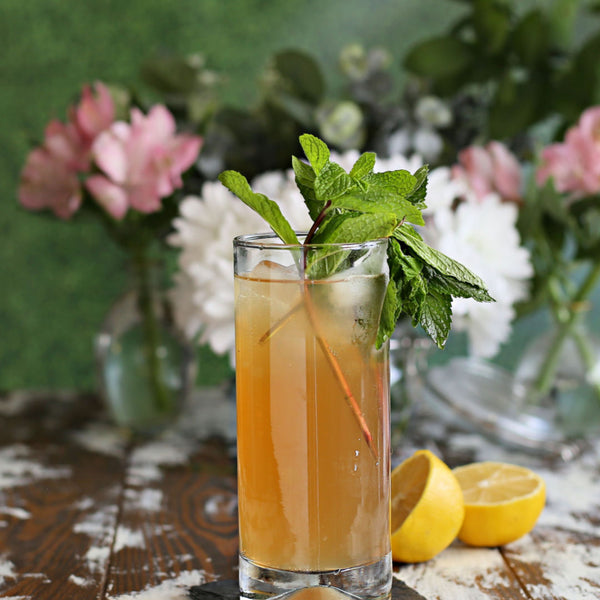 A Garden Party Buck cocktail with bourbon, lemon, Rustic Oak Prohibition Mixer, ginger beer, and fresh mint, served in a tall glass.