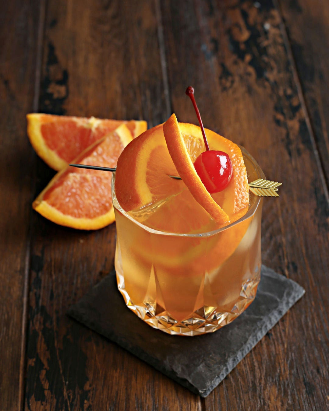 A Brandy Old Fashioned in a rocks glass with Rustic Oak Orange Barrel Aged Mixer, muddled orange, club soda, and a maraschino cherry garnish.