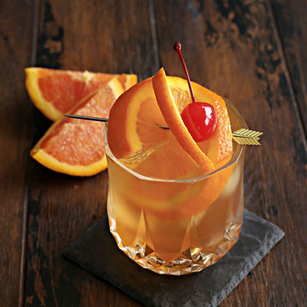 A Brandy Old Fashioned in a rocks glass with Rustic Oak Orange Barrel Aged Mixer, muddled orange, club soda, and a maraschino cherry garnish.