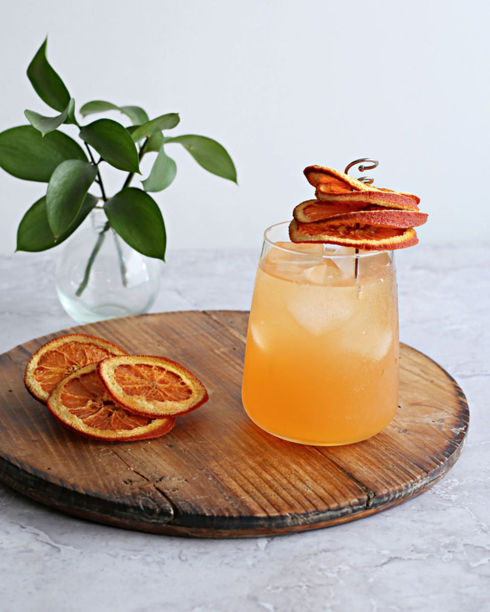 A tall Orange Crush cocktail with vodka, Rustic Oak Orange Barrel Aged Mixer, fresh orange juice, and lemon-lime soda, garnished with an orange slice.