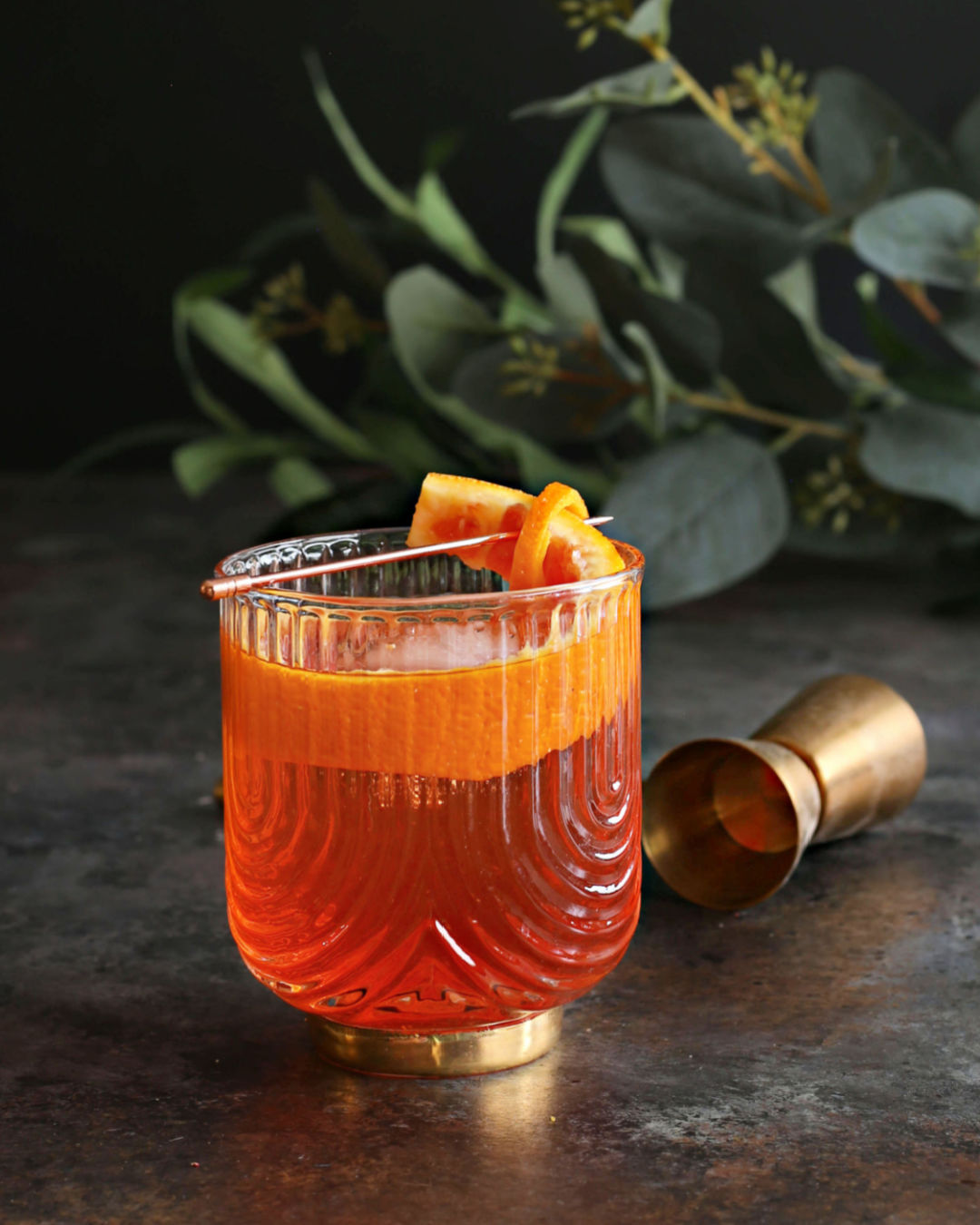 An Orange Negroni cocktail in a rocks glass with an orange peel garnish next to a bottle of Rustic Oak Orange Barrel Aged Old Fashioned Mixer.