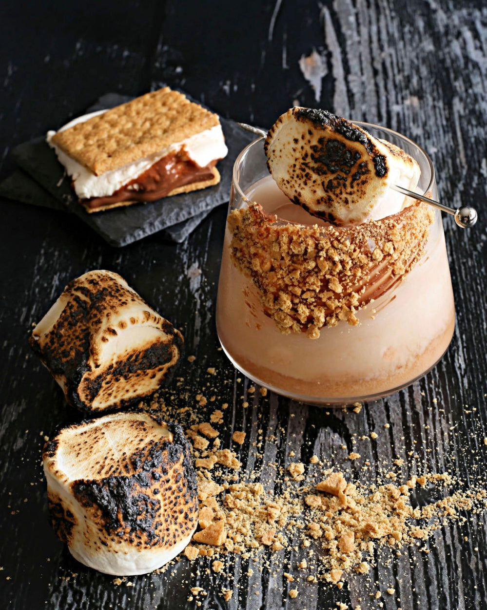 A S'mores Old Fashioned cocktail with bourbon, crème de cacao, and Rustic Oak Barrel Aged Mixer, garnished with chocolate, graham cracker, and marshmallow.