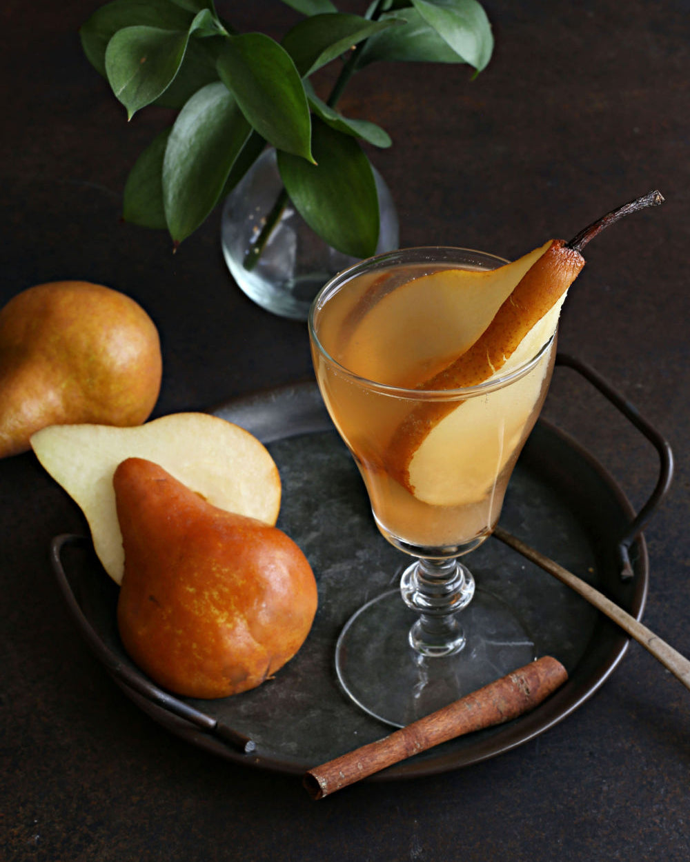 A Spiced Pear Gin Fizz cocktail with gin, pear juice, lemon, Rustic Oak Traditional Mixer, and prosecco, garnished with a pear slice on a dark surface.