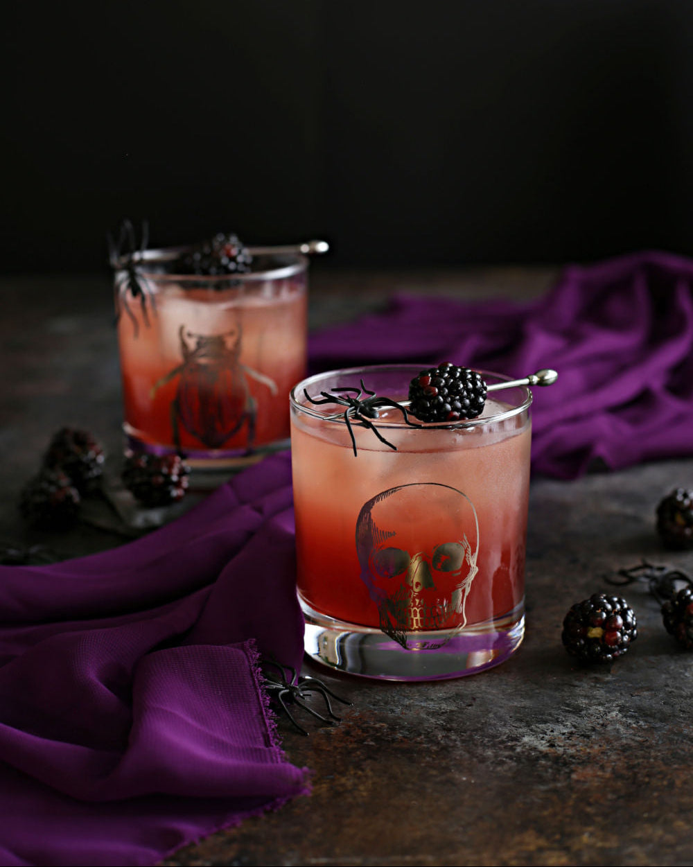 The Black Widow Halloween cocktail with tequila, Rustic Oak Blackberry Mixer, lime juice, and ginger beer, garnished with blackberries on a dark moody surface.