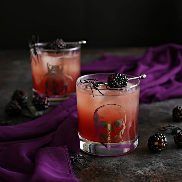 The Black Widow Halloween cocktail with tequila, Rustic Oak Blackberry Mixer, lime juice, and ginger beer, garnished with blackberries on a dark moody surface.